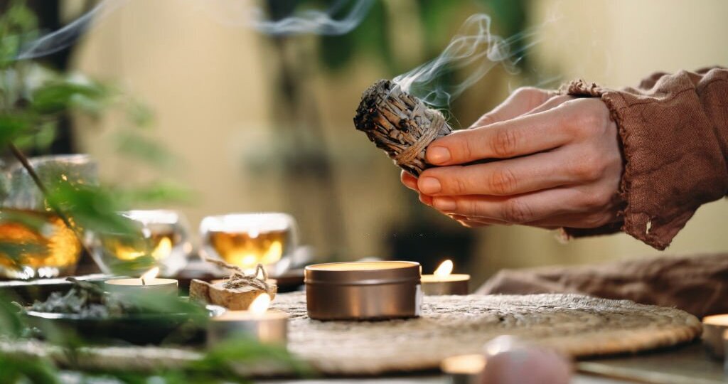 Woman hands burning white sage, before ritual on the table with candles and green plants