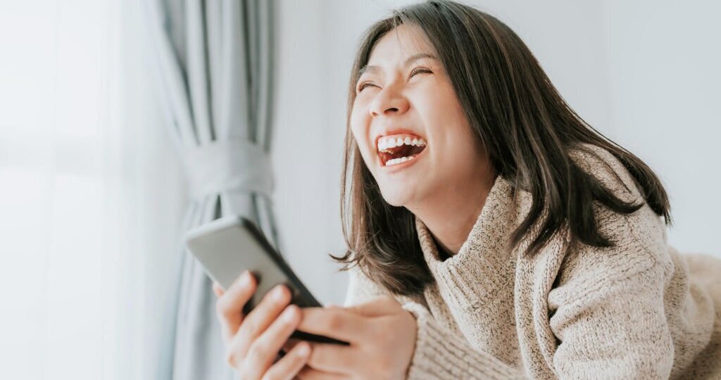 Happy woman laughing while lying on the bed using smartphone mobile at home
