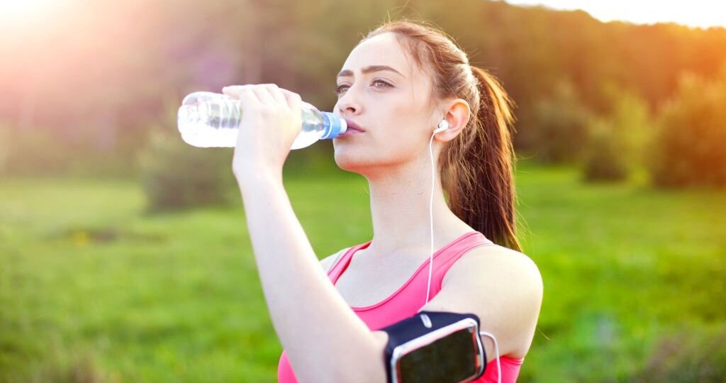 Young brunette drinking water from a bottle after their workout in the nature.