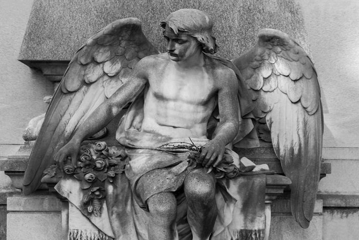 Sculpture of a stone winged angel on a tomb in cemetery. Selective focus