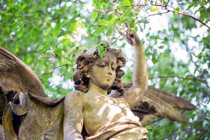 Statue of angel with hand raised in sunlight, from cemetery build in 1864, Czech Republic