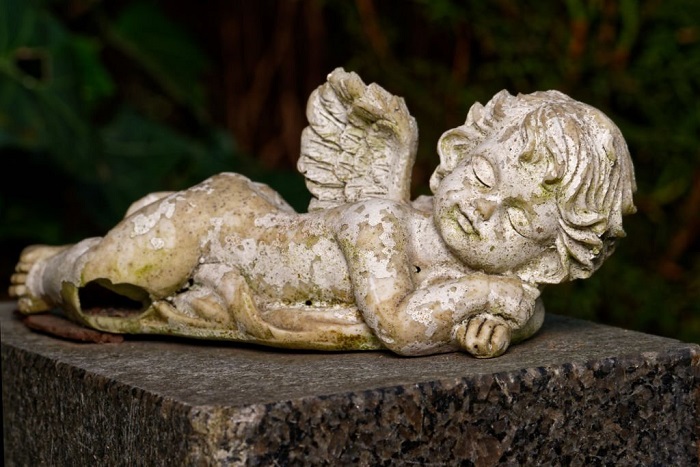 Damaged and weathered small winged angel lies on tombstone