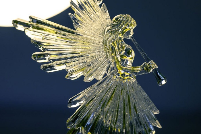 A golden transparent angel blowing a horn with a light source behind