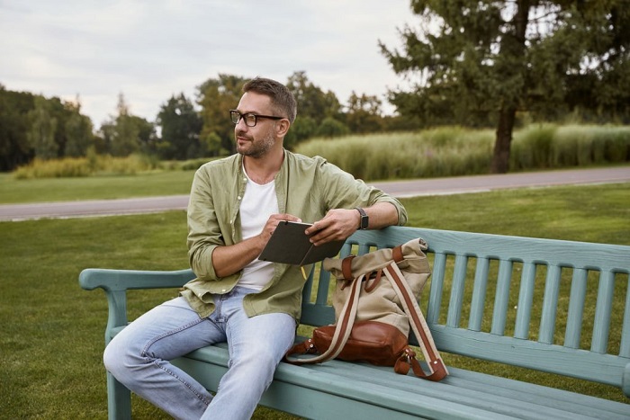 Axel wearing eyeglasses sitting on the wooden bench in park 