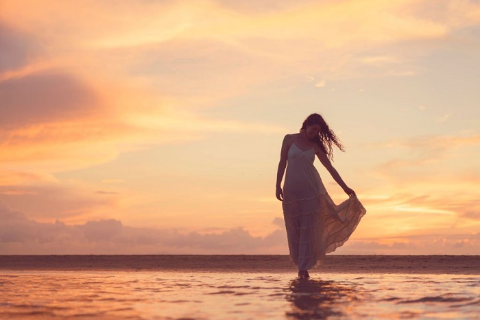 Silhouette of Blair walking down the beach against sunset