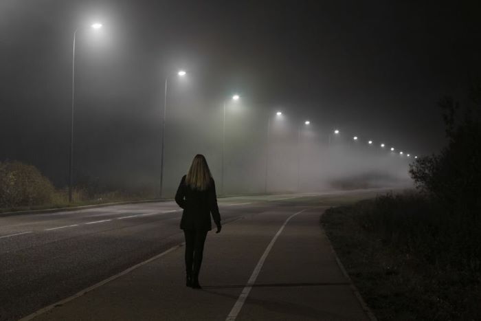 Emily alone slowly walking under white street lights in night