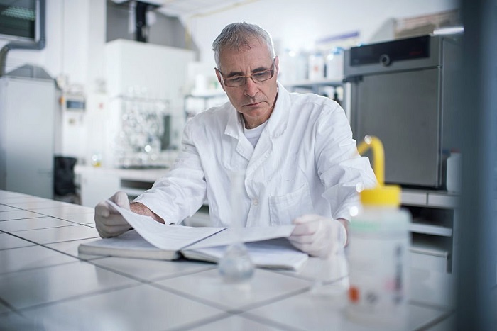 Male scientist sitting in laboratory and reading medical documents from a book