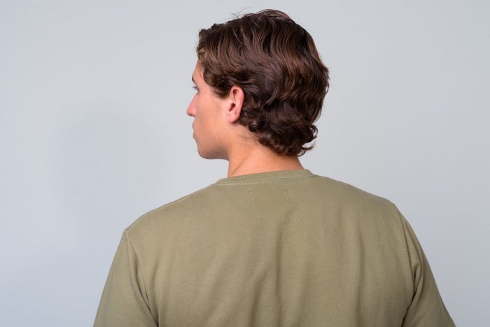 Studio shot of Myles with wavy hair wearing green shirt against white background