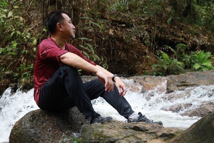 Portrait of Samuel sitting on a rock and enjoying view of a waterfall in a tropical rainforest