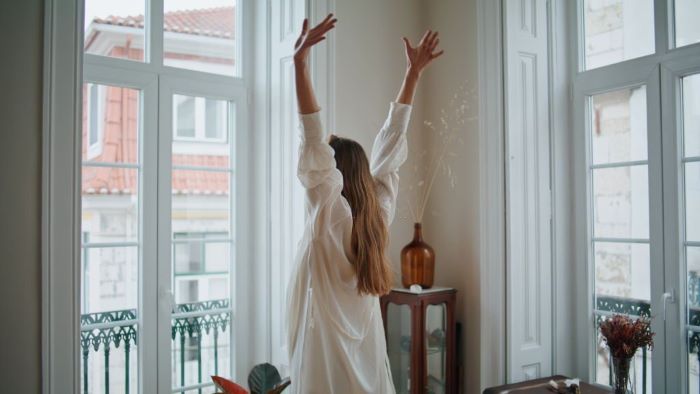 Sarah stretching arms at window interior closeup