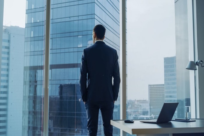 Back view of Tobias wearing a suit standing in his office