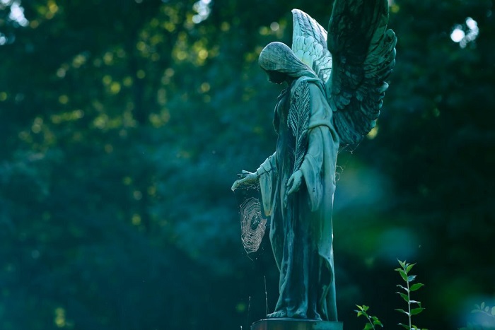 Weathered old copper angel statue with a spider web on a cemetery in Germany