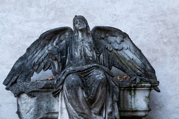 An angel statue sitting on a bench attached to the face of a building