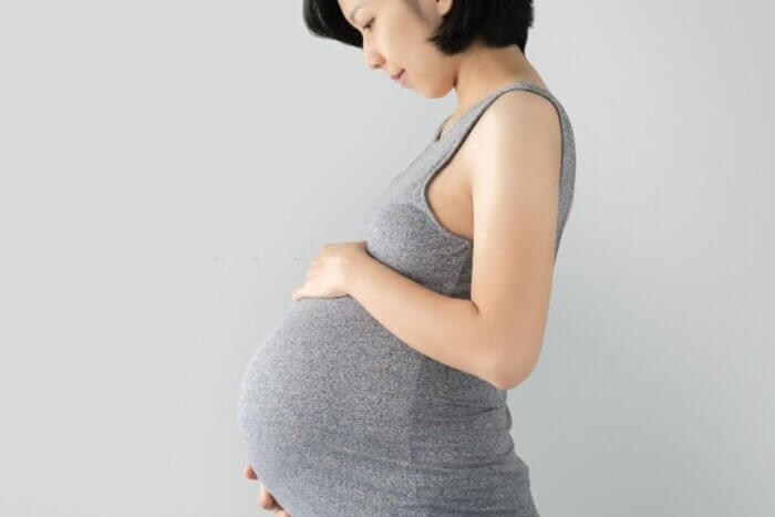 Pregnant woman standing and touching big belly with her hands