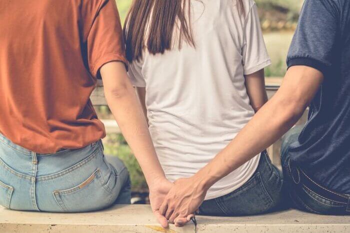 Boyfriend and another woman grab hands from behind together without sight of his girlfriend