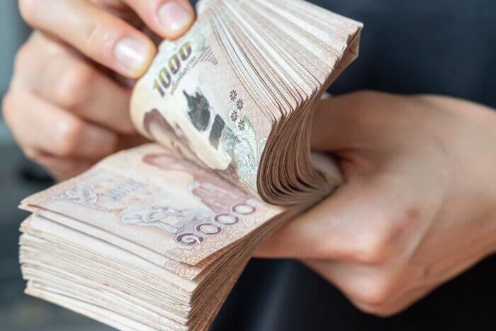 Close up of someone hands counting a pile of one thousand Thai baht